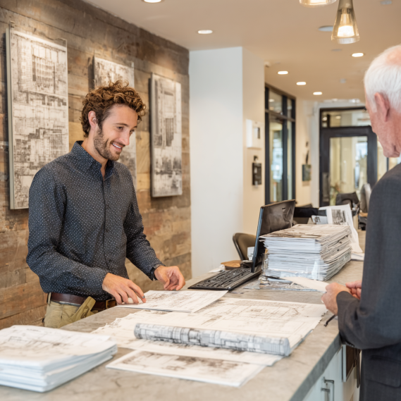 A close-up of hands handing over official documents and a site plan to a permit clerk.