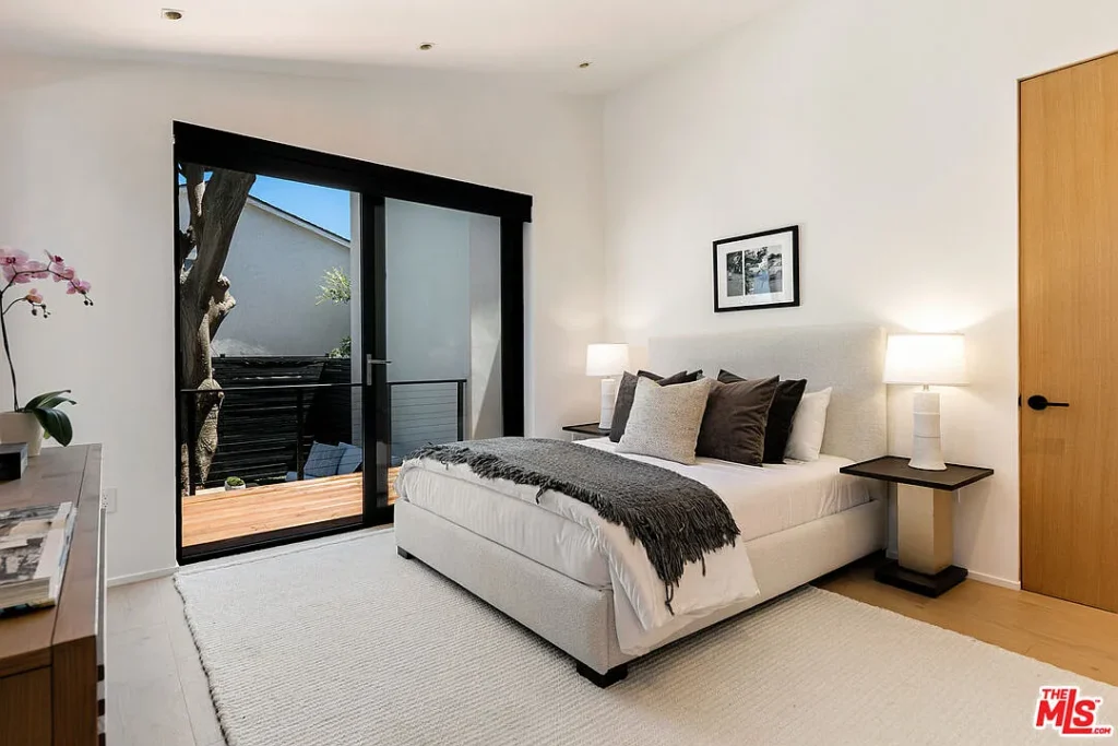 Modern bedroom interior at 2202 California Ave in Santa Monica featuring a minimalist bed design, black framed glass doors, natural light and contemporary finishes